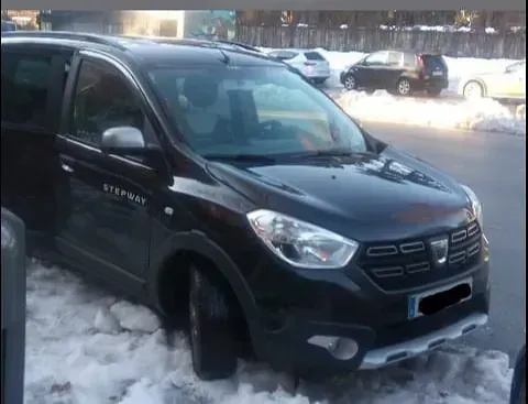 Dacia Dokker Stepway negro aparcado sobre la nieve cerca de una calle. Detalles en gris, en un entorno urbano nevado.