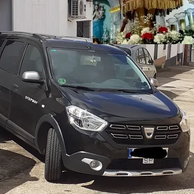 Dacia Dokker Stepway negro estacionado al aire libre con un fondo borroso que incluye una figura religiosa.
