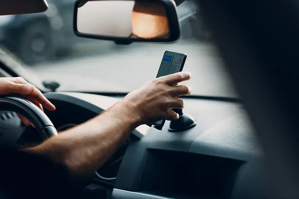 Persona con un teléfono inteligente en un coche. El teléfono está montado en el salpicadero y la mano del conductor está en el volante.
