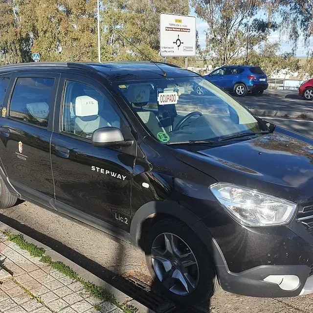 Taxi Dacia Duster Stepway negro estacionado en una calle junto a un bordillo, con otros coches y una señal de tráfico al fondo.