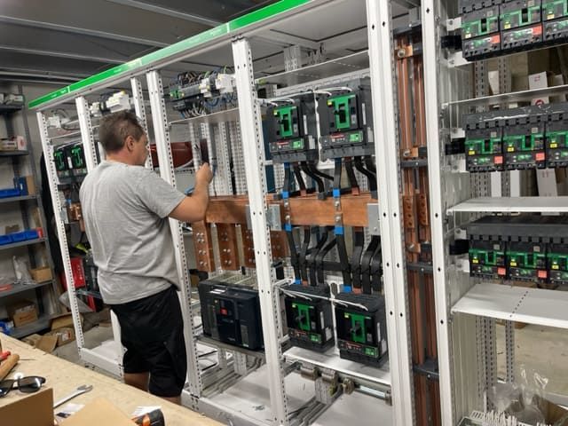 Un hombre está trabajando en un panel eléctrico en una fábrica.