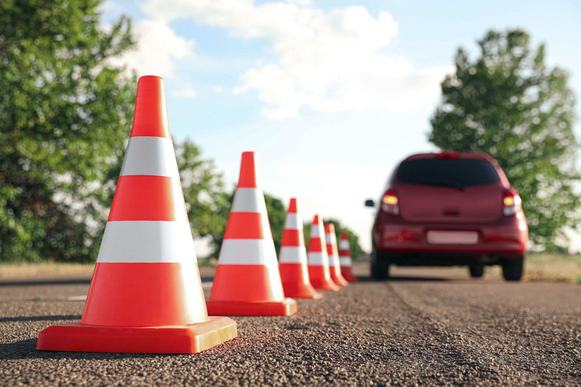 Un coche rojo circula por una carretera al lado de una hilera de conos de tráfico.