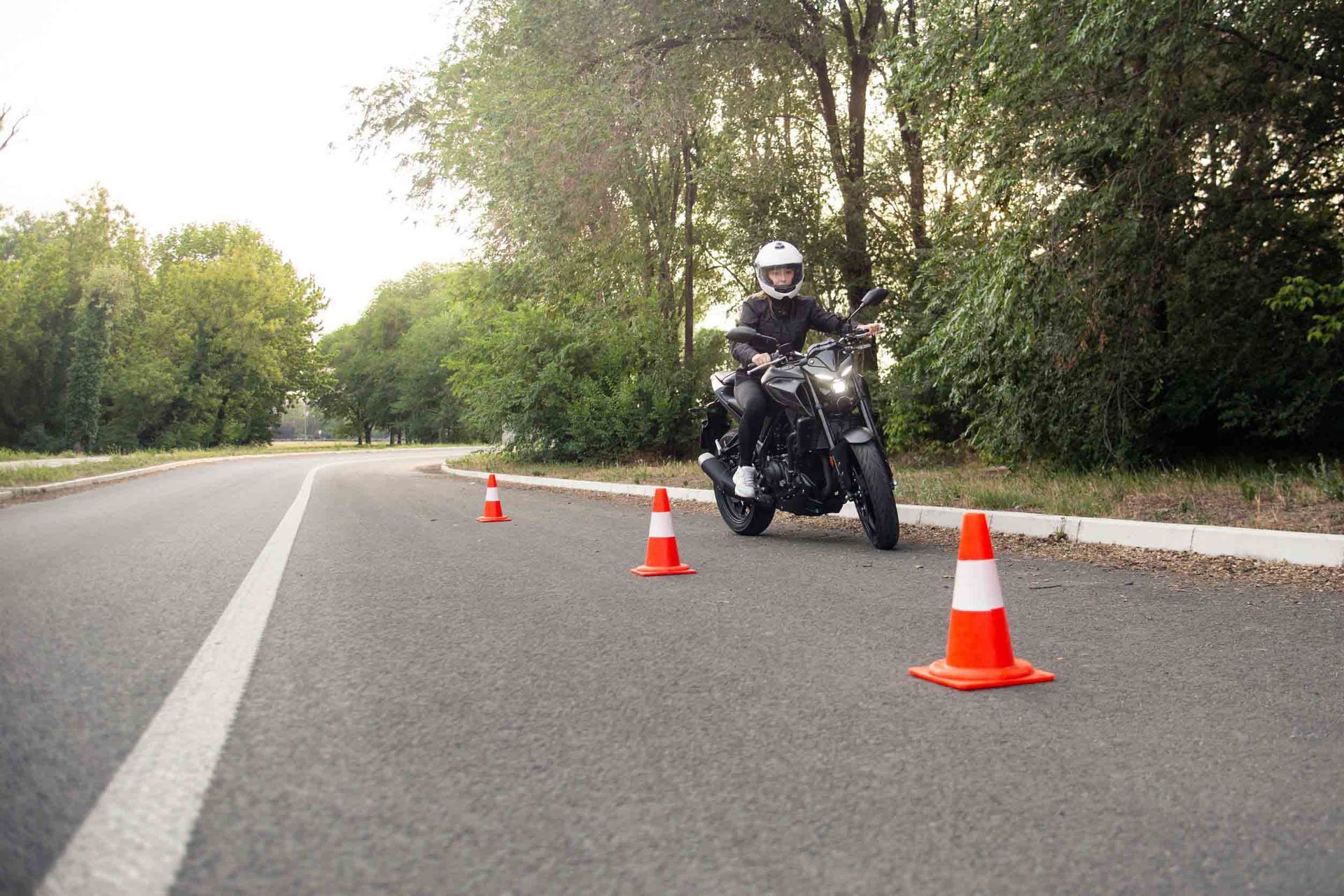 Un hombre conduce una motocicleta por una carretera al lado de conos de tráfico.