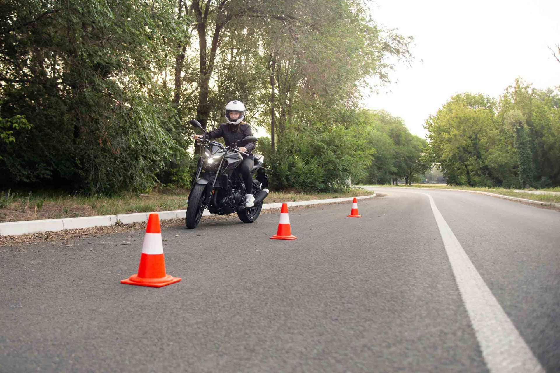 Un hombre conduce una motocicleta por una carretera al lado de conos de tráfico.