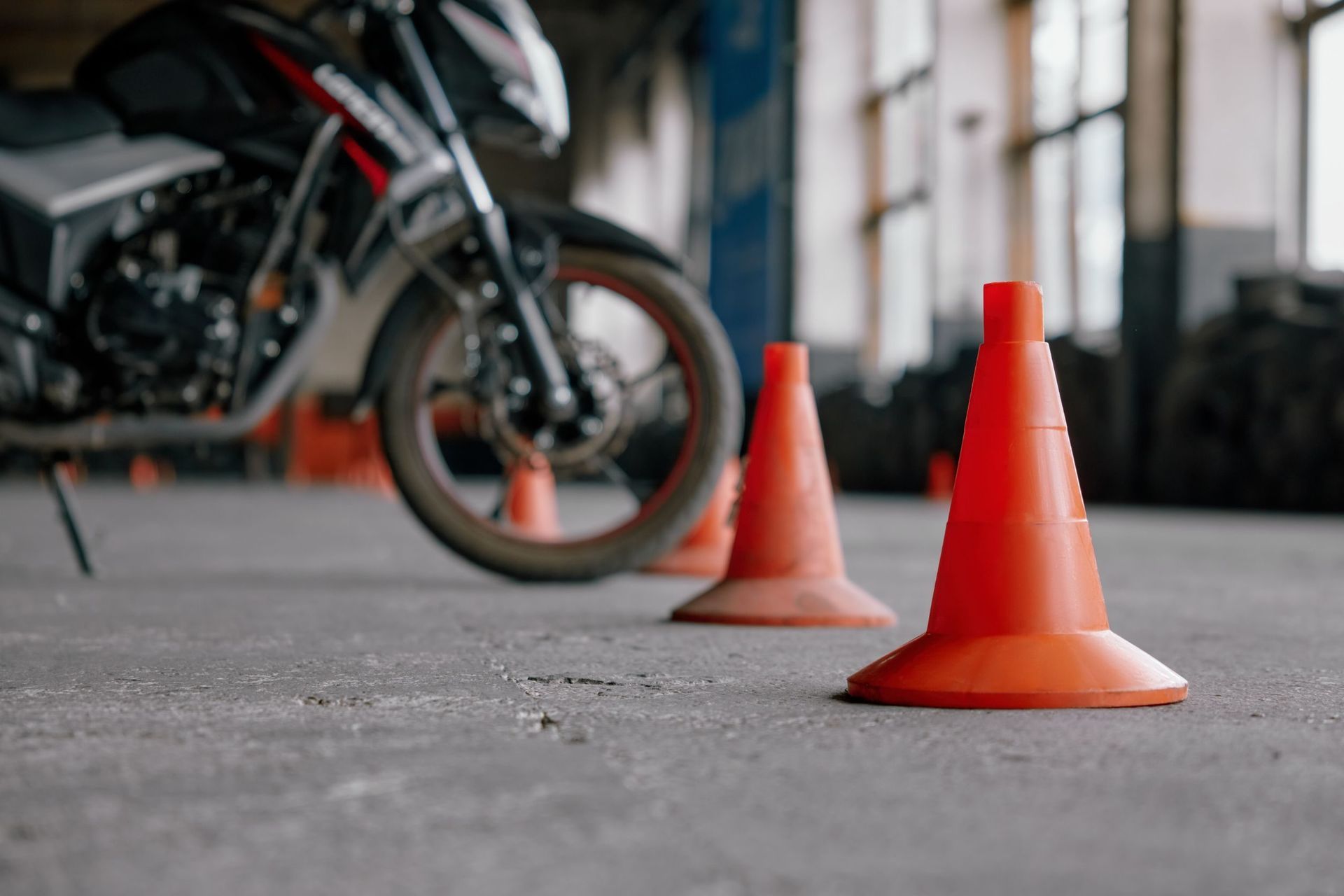 Una motocicleta está estacionada al lado de una fila de conos de tráfico naranjas.