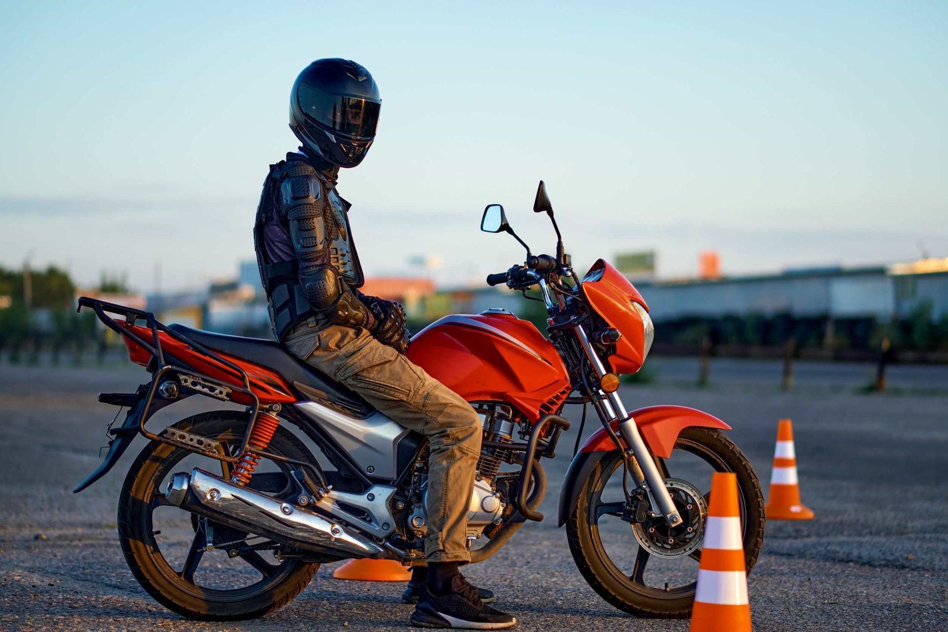 Un hombre está sentado en una motocicleta roja al lado de conos de tráfico.