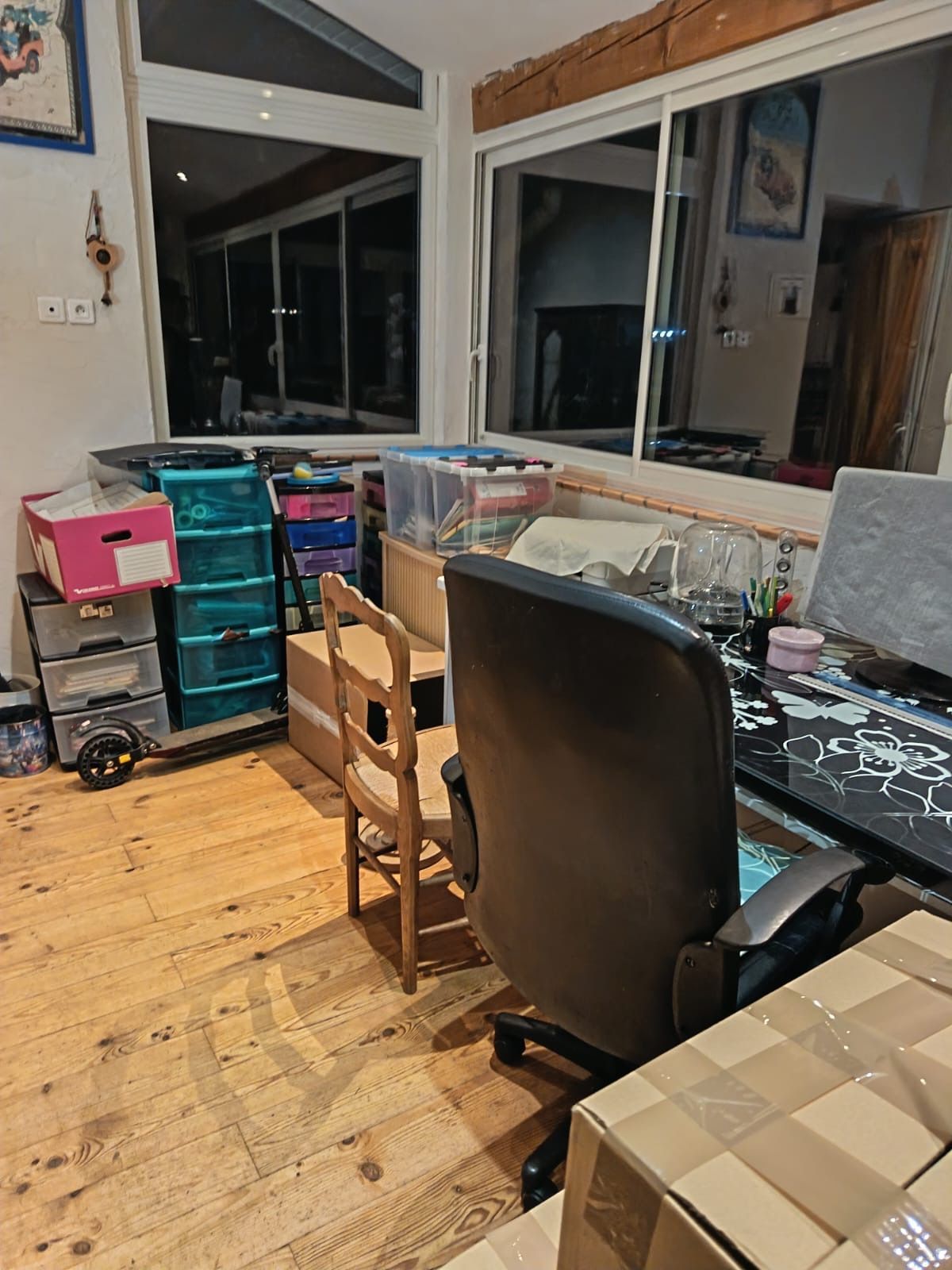 Pièce encombrée avec bureaux, écran d'ordinateur, chaise noire et boîtes de rangement.