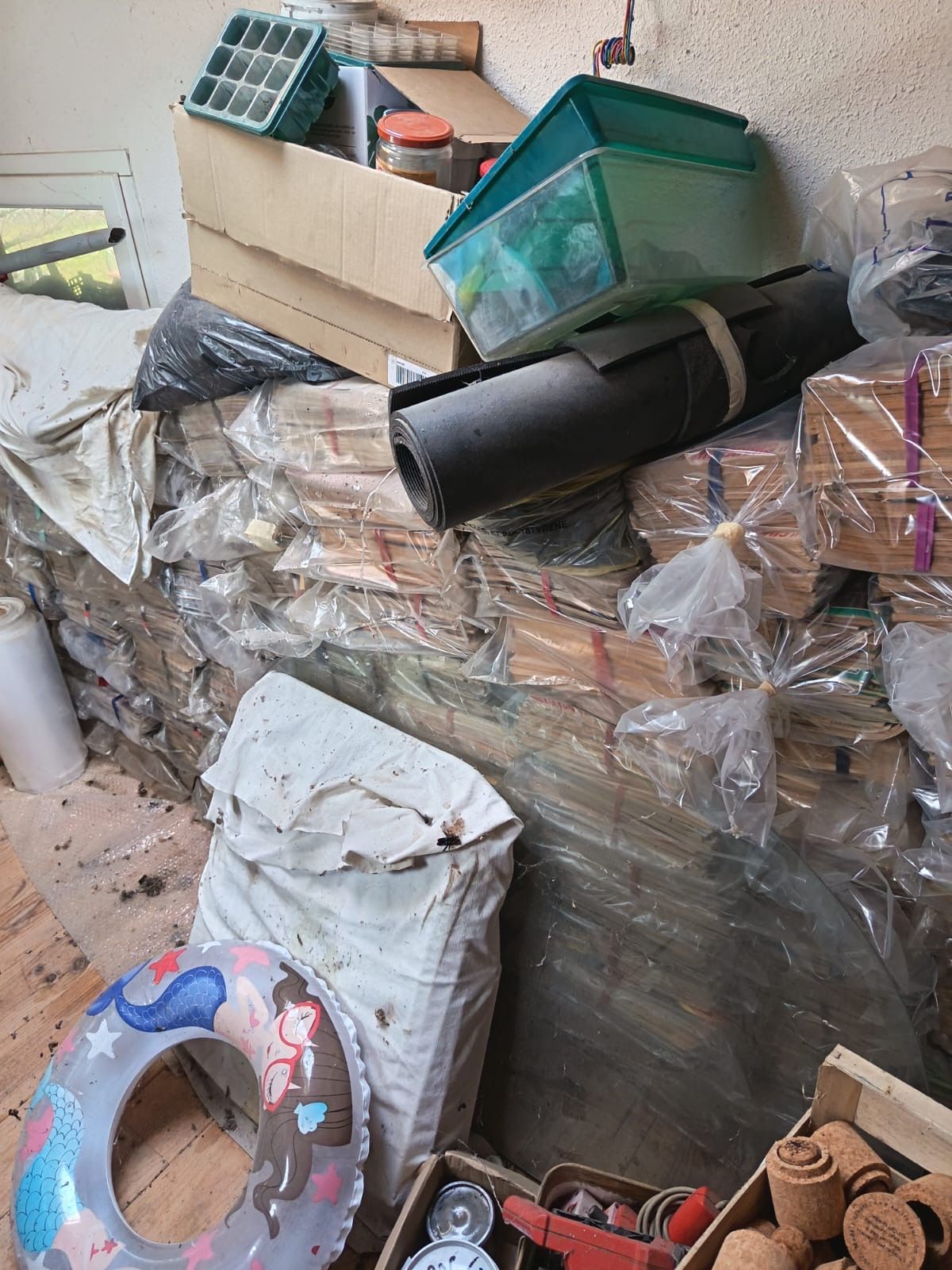 Zone de stockage encombrée de sacs-poubelle empilés, de cartons et d'objets divers.