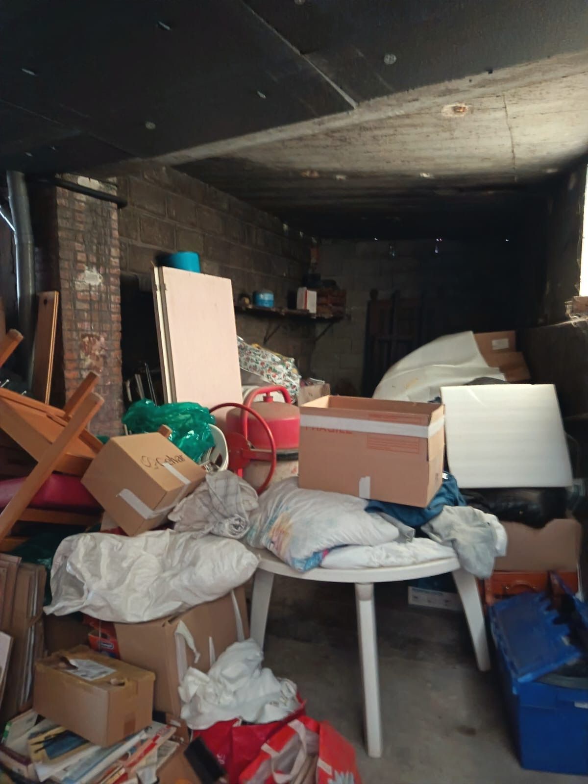 Garage ou débarras encombré de cartons, de sacs et de meubles.