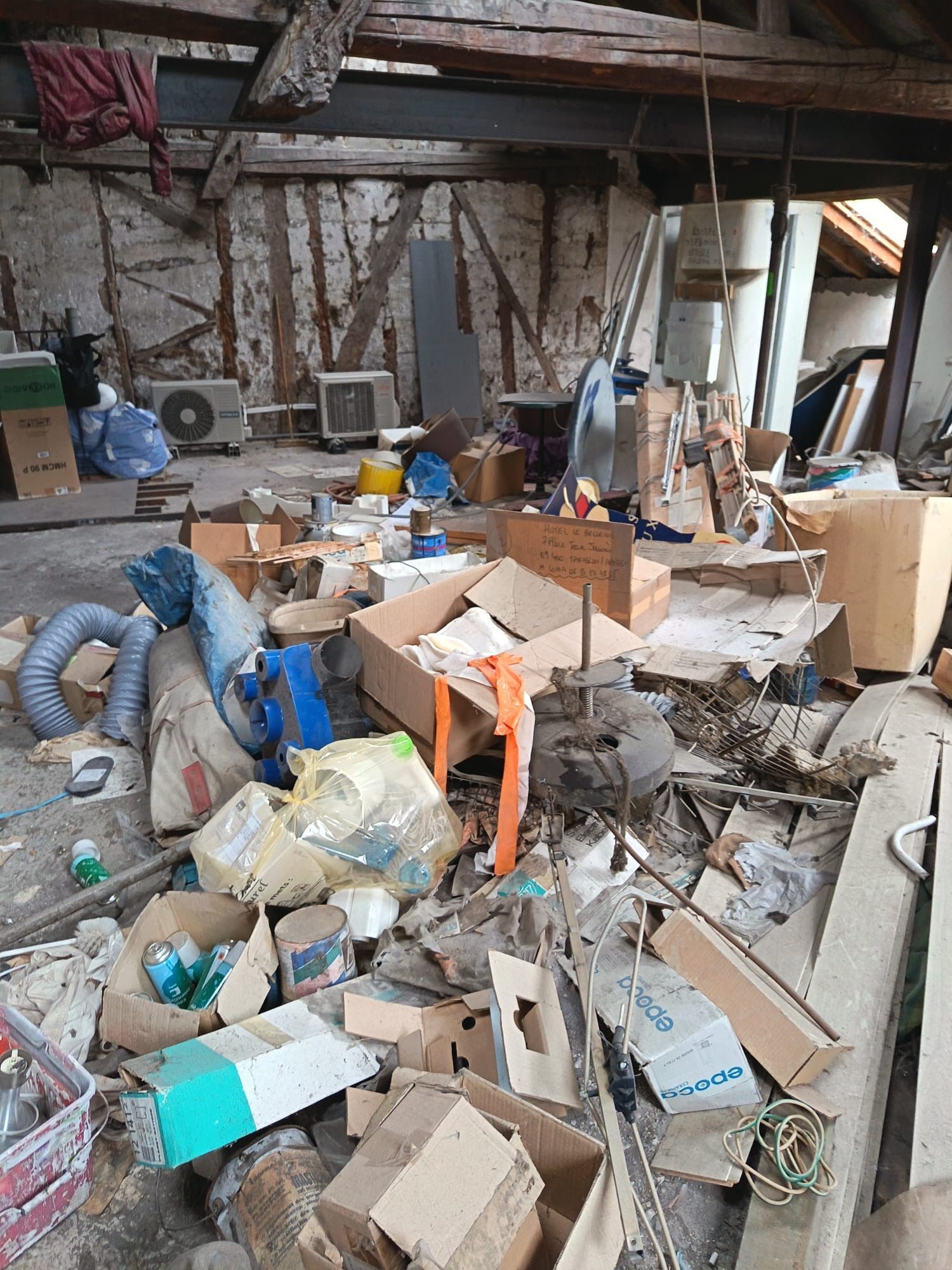 Des combles encombrés de piles de cartons, d'outils et de débris éparpillés sur le sol.