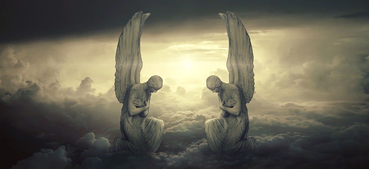 Dos ángeles de piedra se arrodillan en un cielo nublado y resplandeciente, mirándose el uno al otro con las alas extendidas.