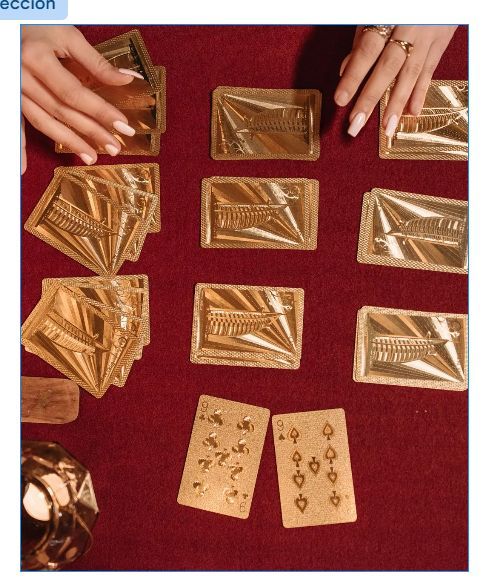 Manos colocando tarjetas de papel de oro sobre un paño rojo, con dos cartas de juego en la parte inferior.