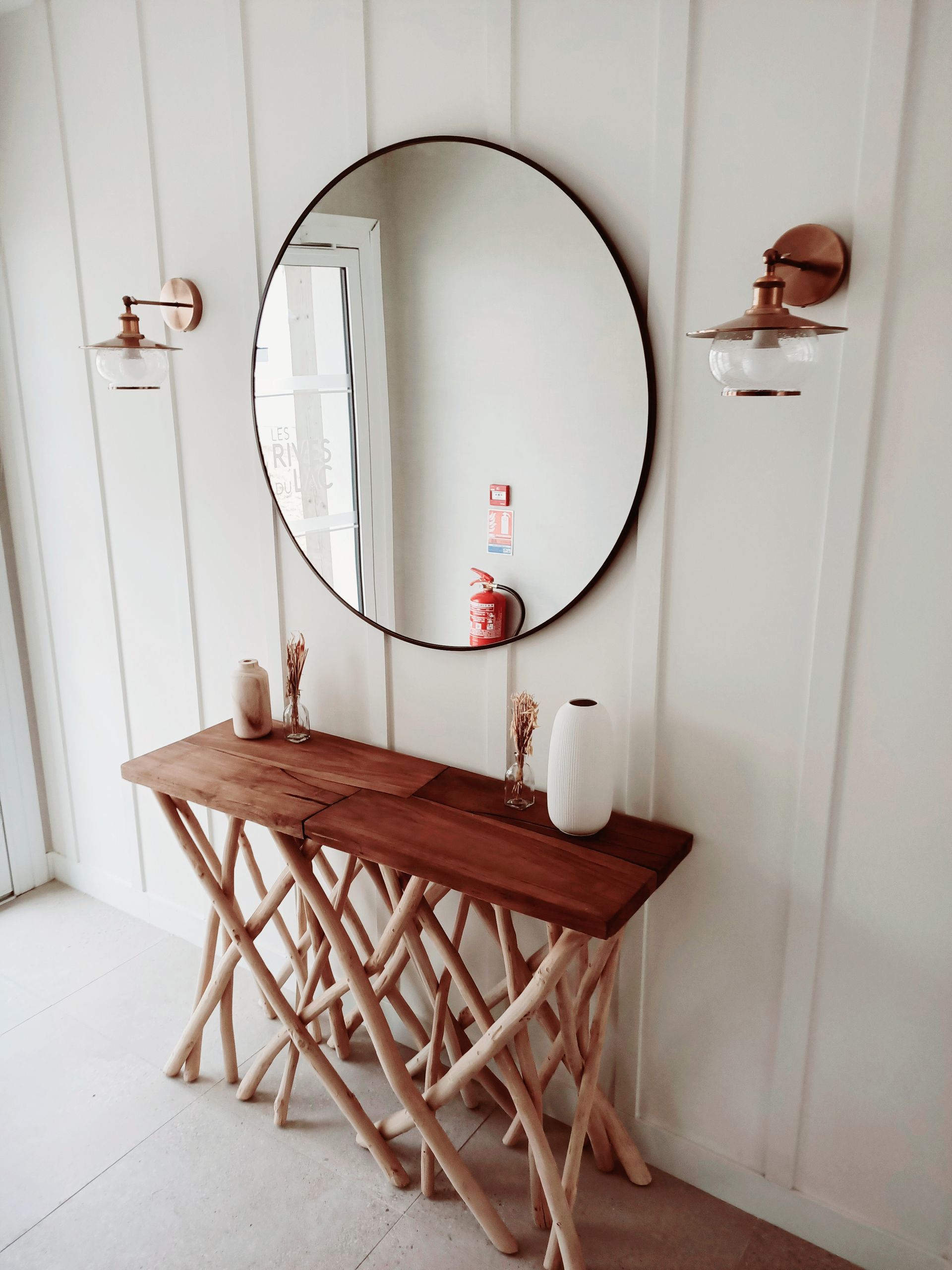 Un miroir rond est suspendu au-dessus d'une table en bois dans un couloir.