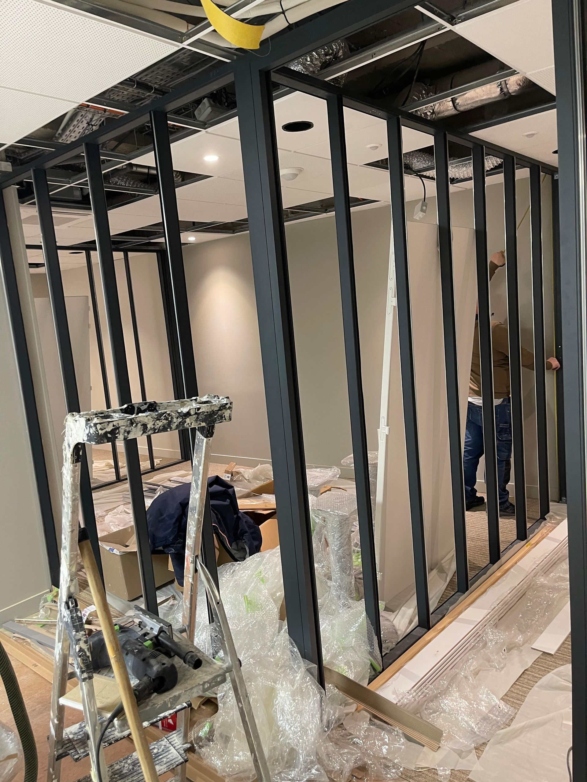 Chantier de construction intérieure avec structure métallique noire. Des ouvriers assemblent une pièce.