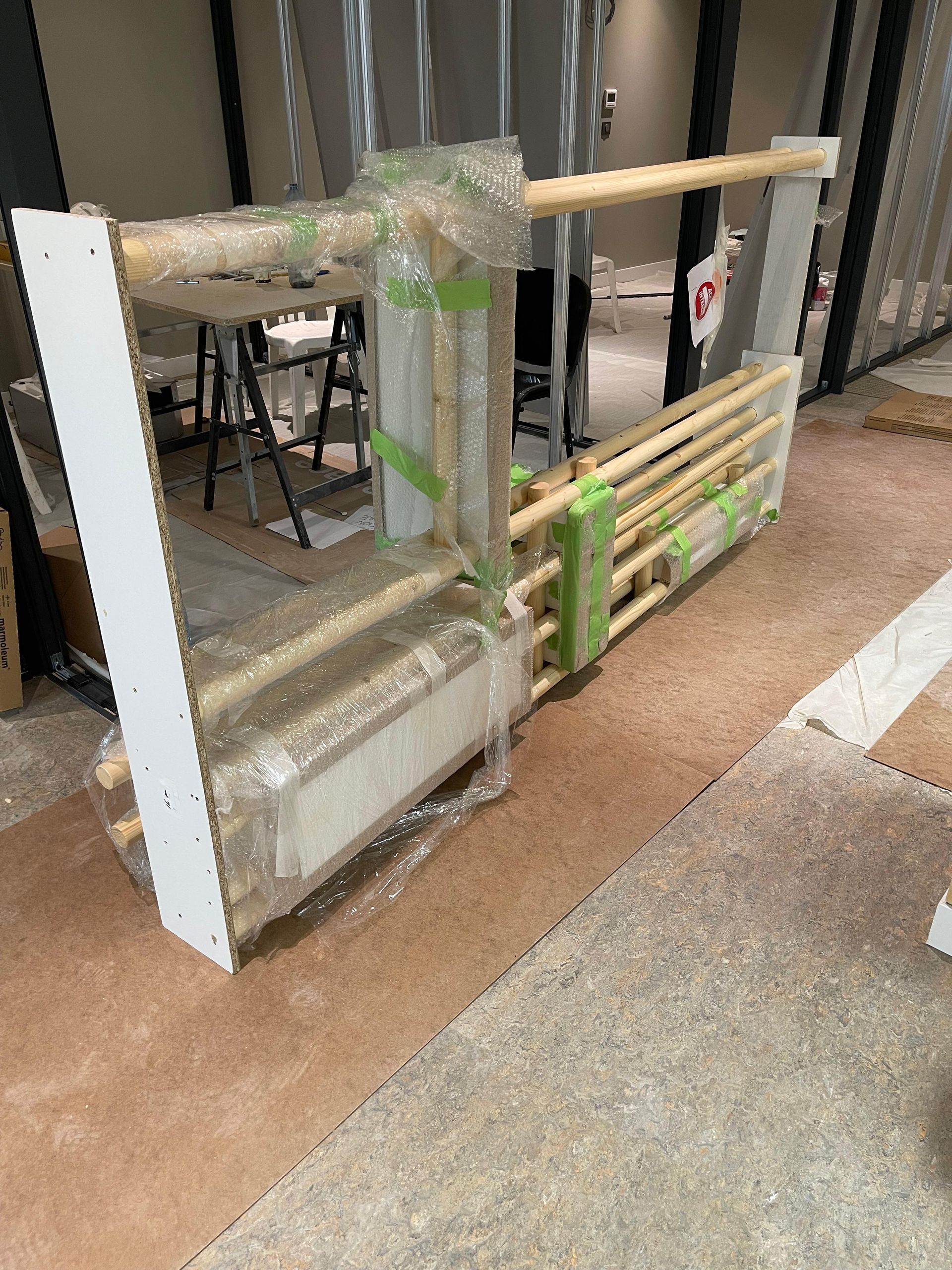 Barrière de bois et barrière blanche enveloppée de plastique sur un sol brun, probablement en construction.