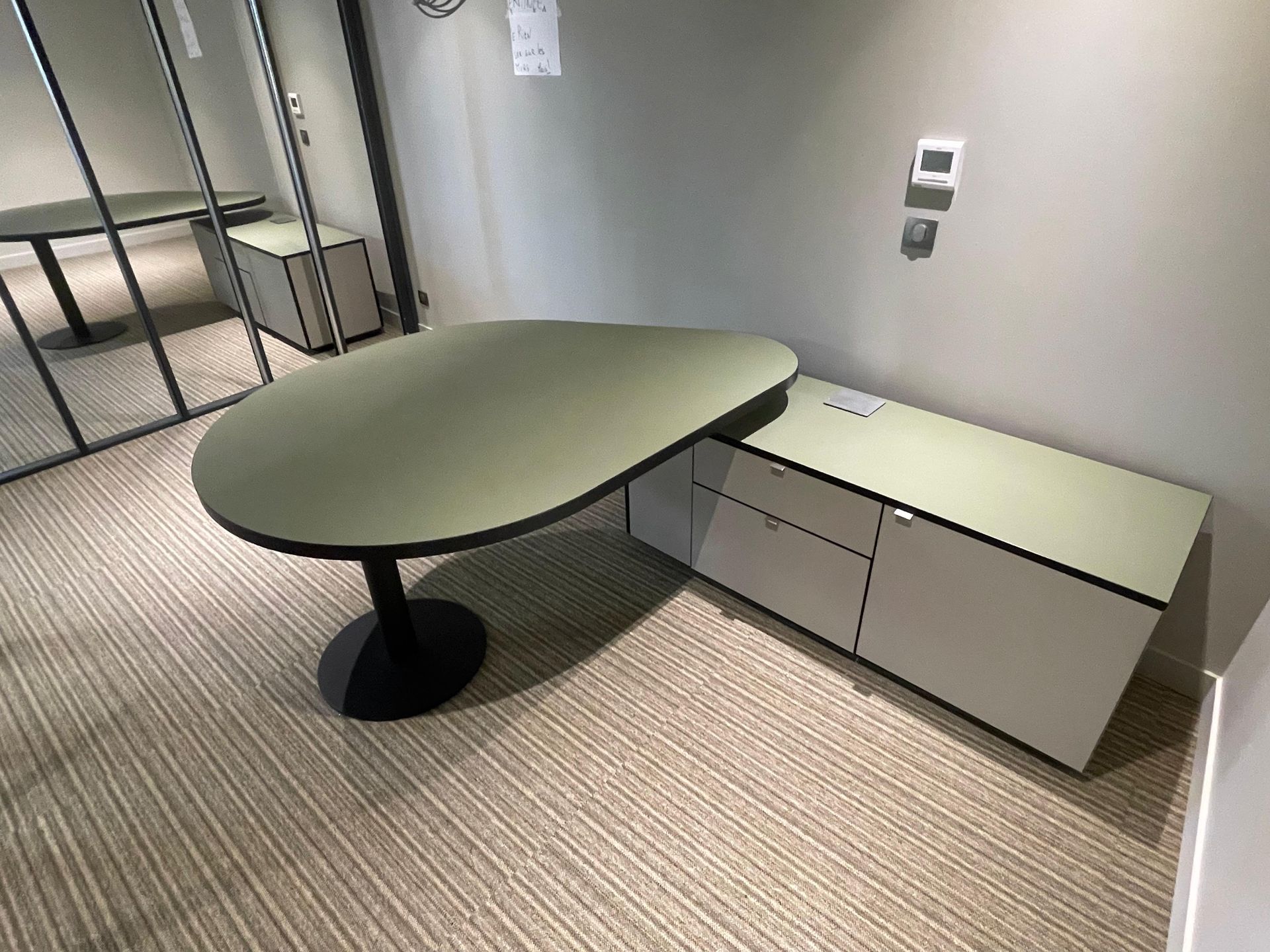 Bureau avec plateau vert, armoire blanche, piètement noir et moquette beige.