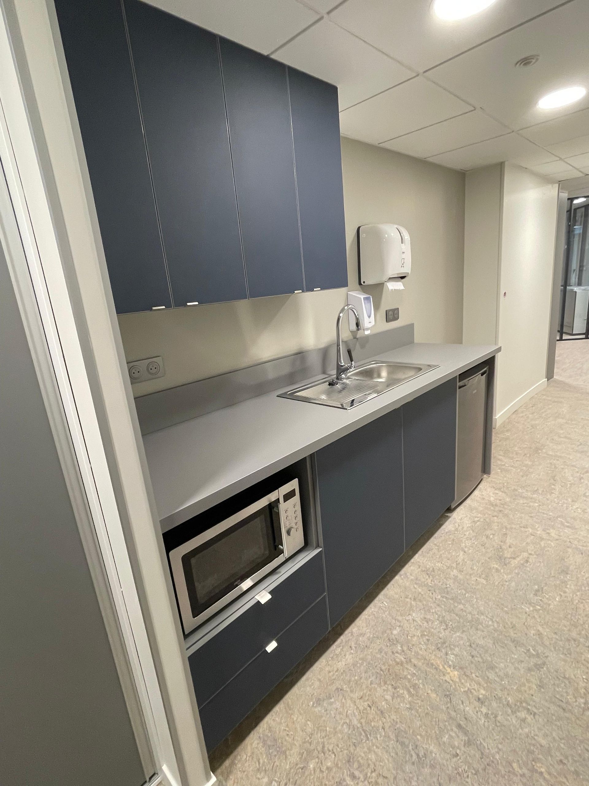 Kitchenette bleu foncé avec placards, évier, micro-ondes et mini-réfrigérateur.