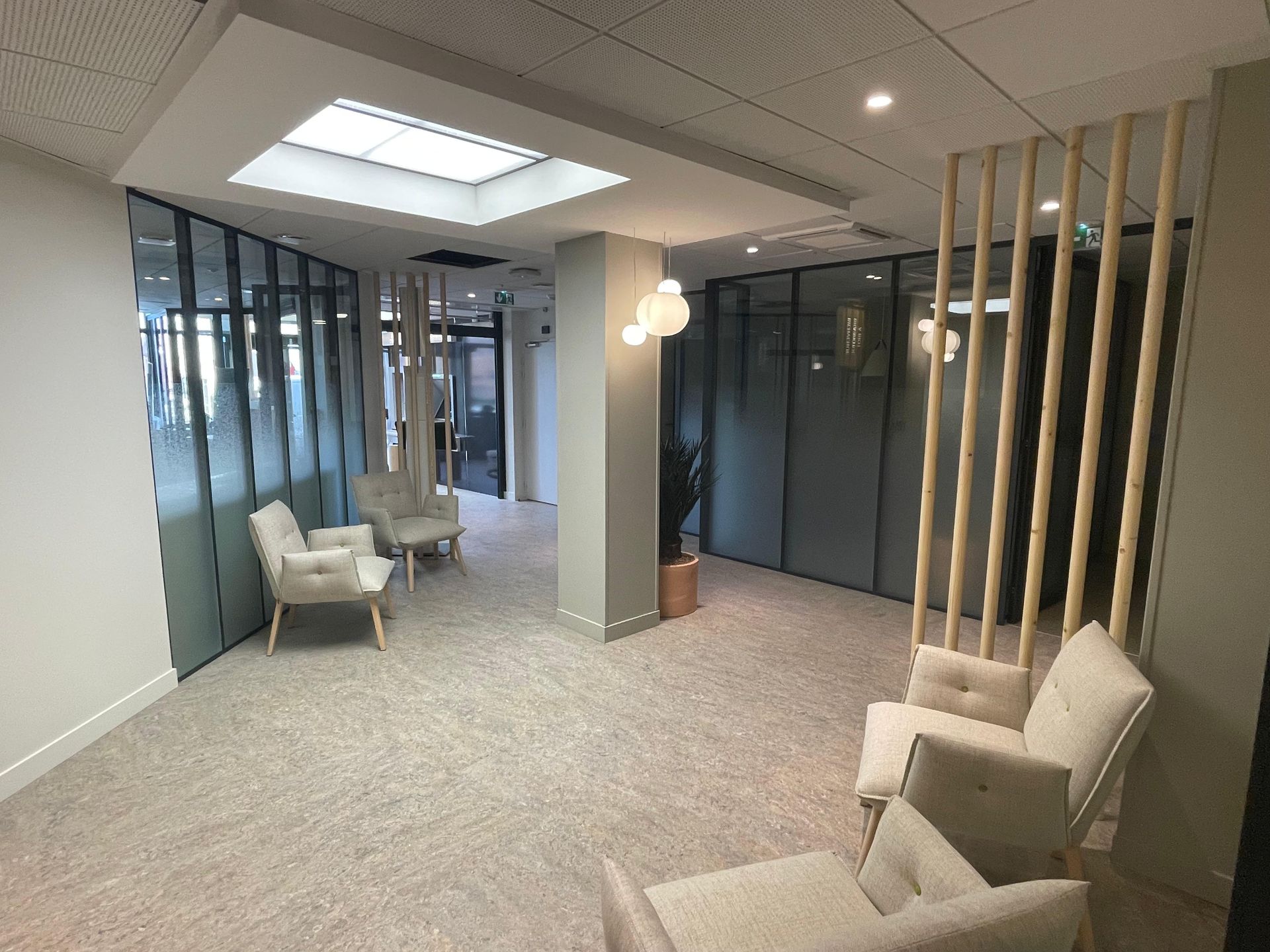 Salle d'attente moderne avec fauteuils, parois vitrées et puits de lumière.