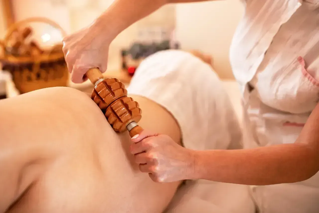 Persona que recibe un masaje de maderoterapia en la espalda por parte de otra persona que sostiene una herramienta de masaje de madera.