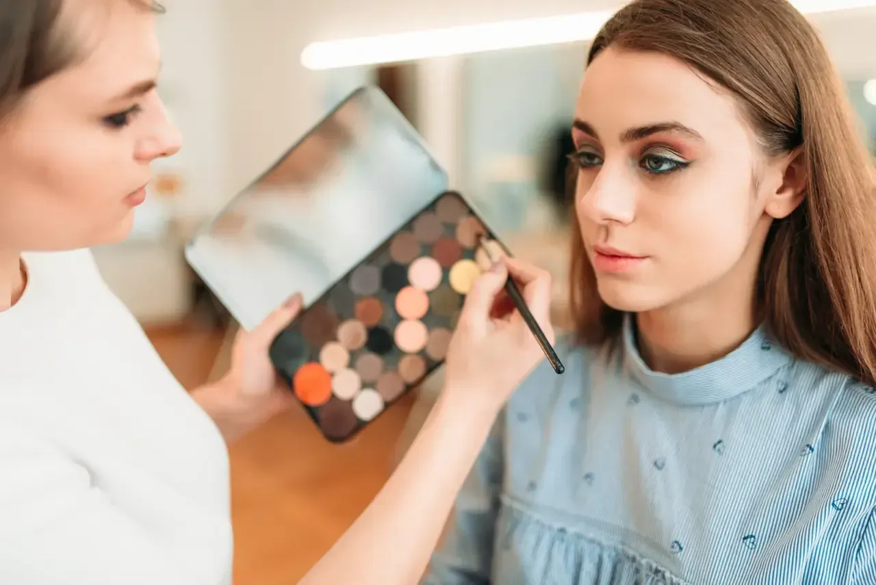 Maquilladora aplicando sombra de ojos a una clienta en un salón de belleza.