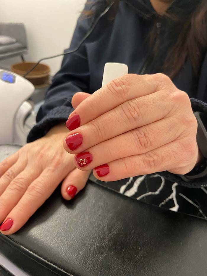 Manos con esmalte de uñas rojo, una uña con diseño dorado, cerca de una luz ultravioleta.