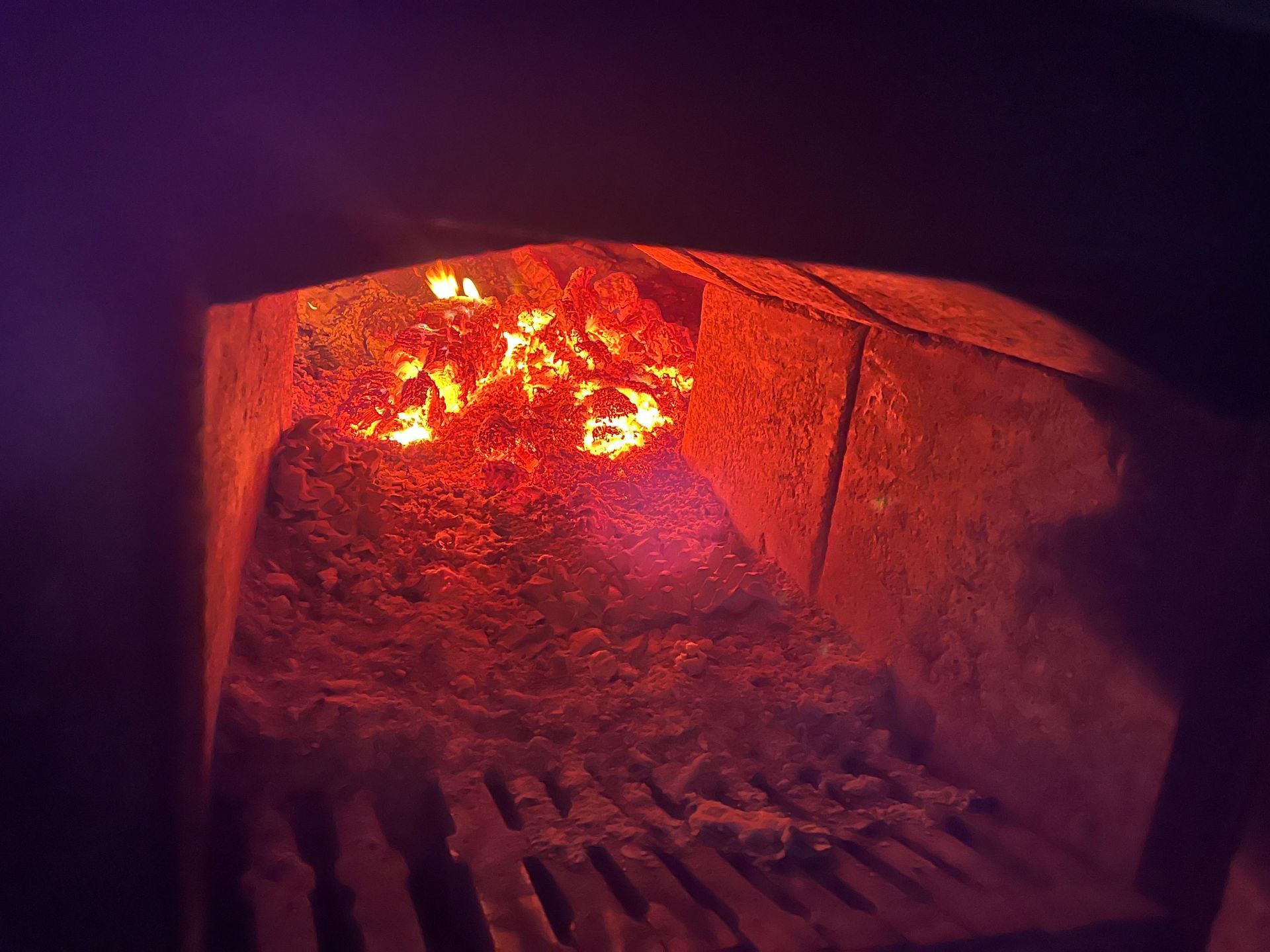 Fuego ardiente dentro de un horno oscuro con una rejilla de metal en la parte inferior.
