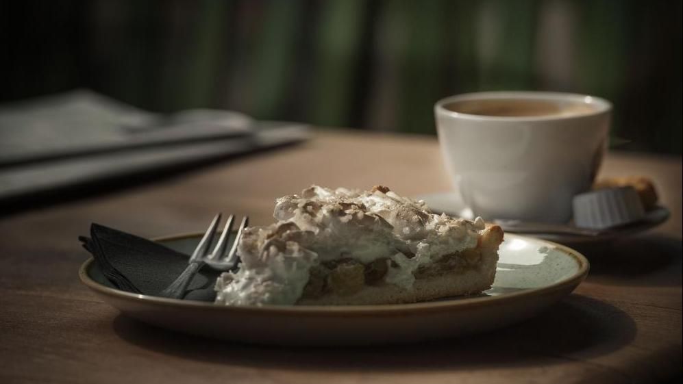 Er ligt een stuk taart op een bord naast een kopje koffie.