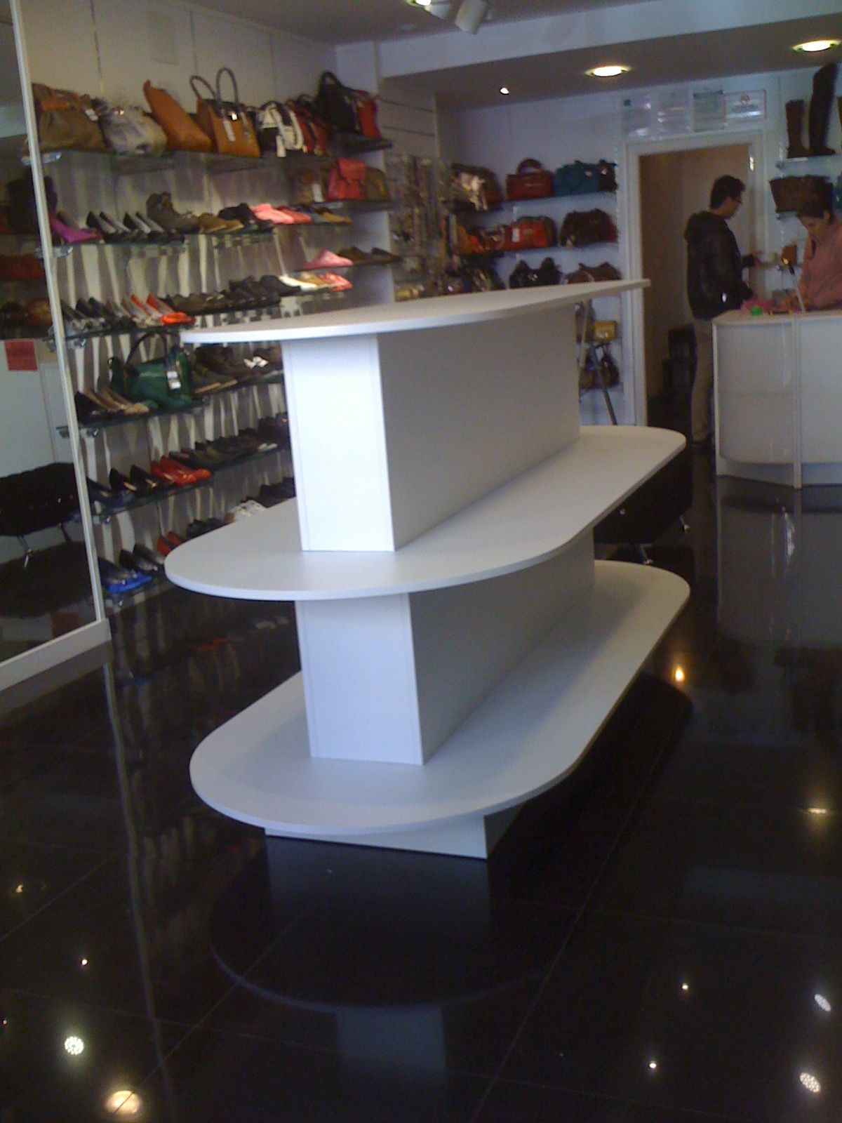 Interior de una boutique de zapatos con estanterías blancas y filas de zapatos coloridos a lo largo de las paredes.