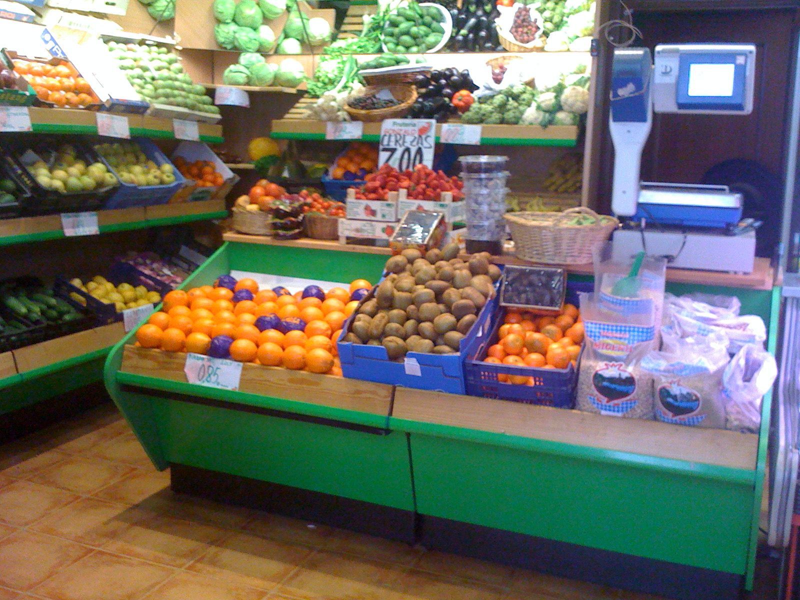 Sección de frutas y verduras con naranjas, kiwis y plátanos en un expositor de supermercado.