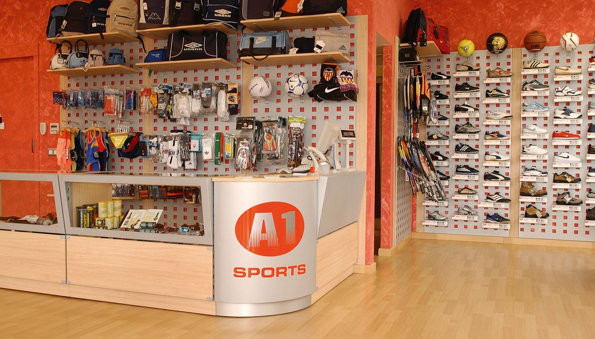 Interior de una tienda de deportes con zapatos, accesorios y un mostrador blanco con un logotipo naranja.