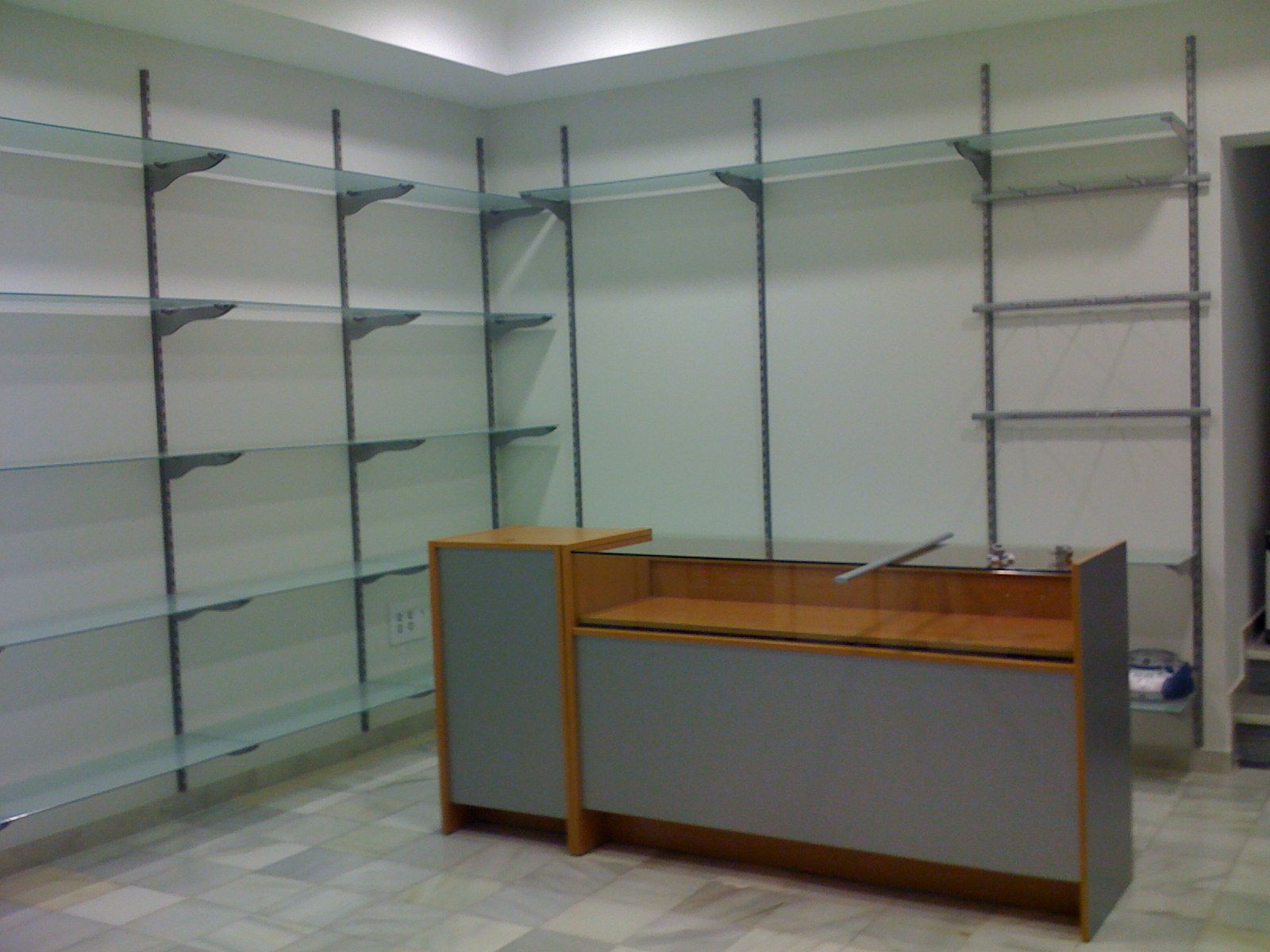 Local comercial vacío con estanterías de cristal y un mostrador de madera en el centro.
