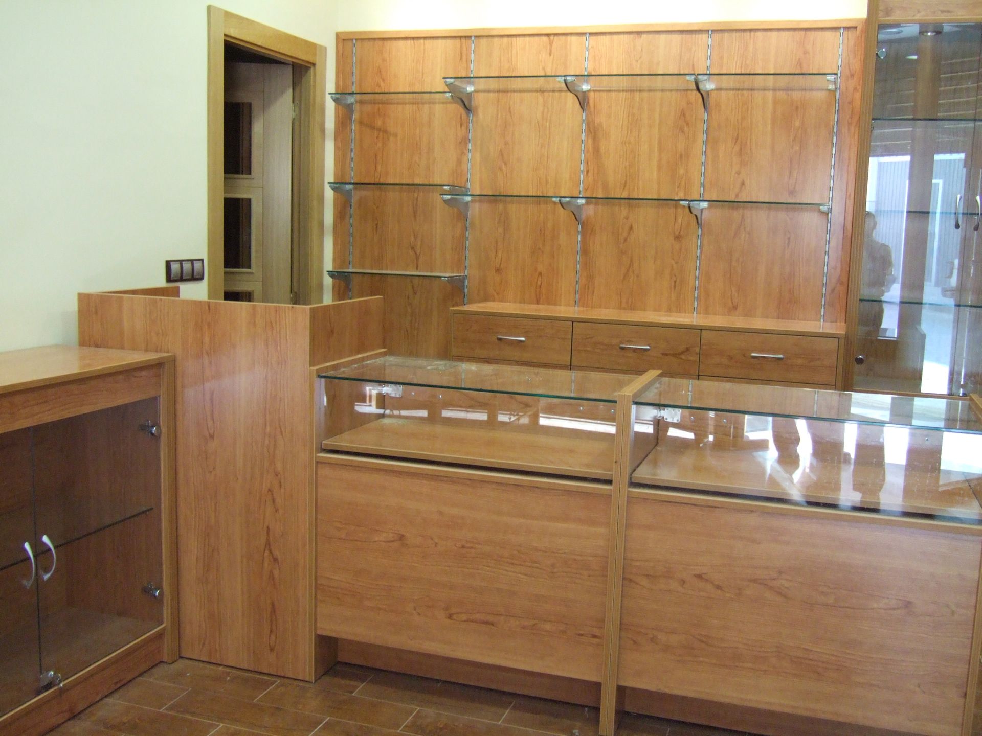 Mostrador de venta vacío con armarios de madera y estantes de cristal en una habitación luminosa.