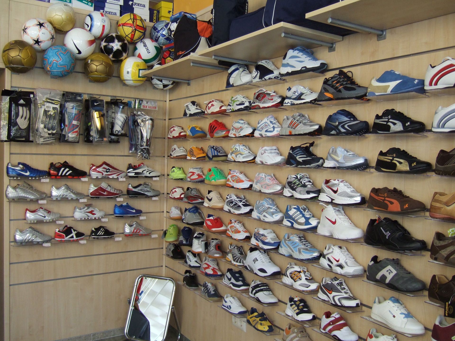 Pared de una zapatería con filas de zapatillas deportivas y balones deportivos expuestos en estantes.