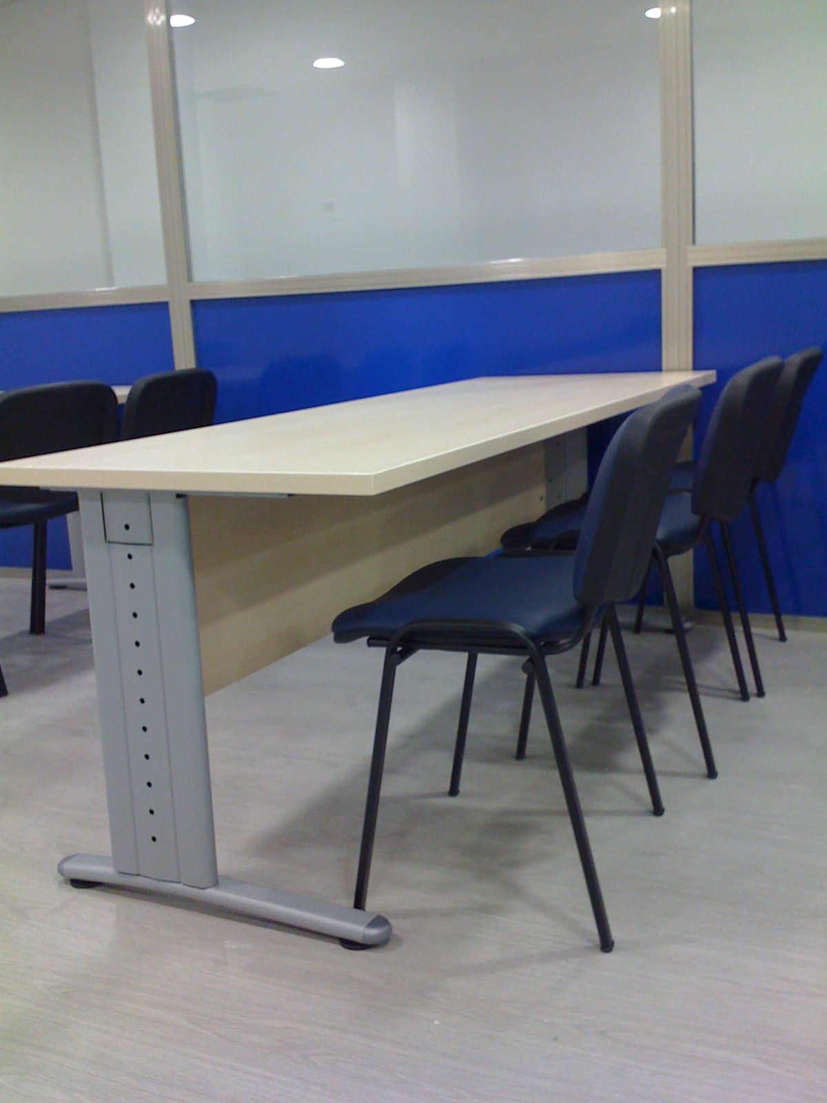 Sala de reuniones vacía con una mesa blanca y sillas negras.