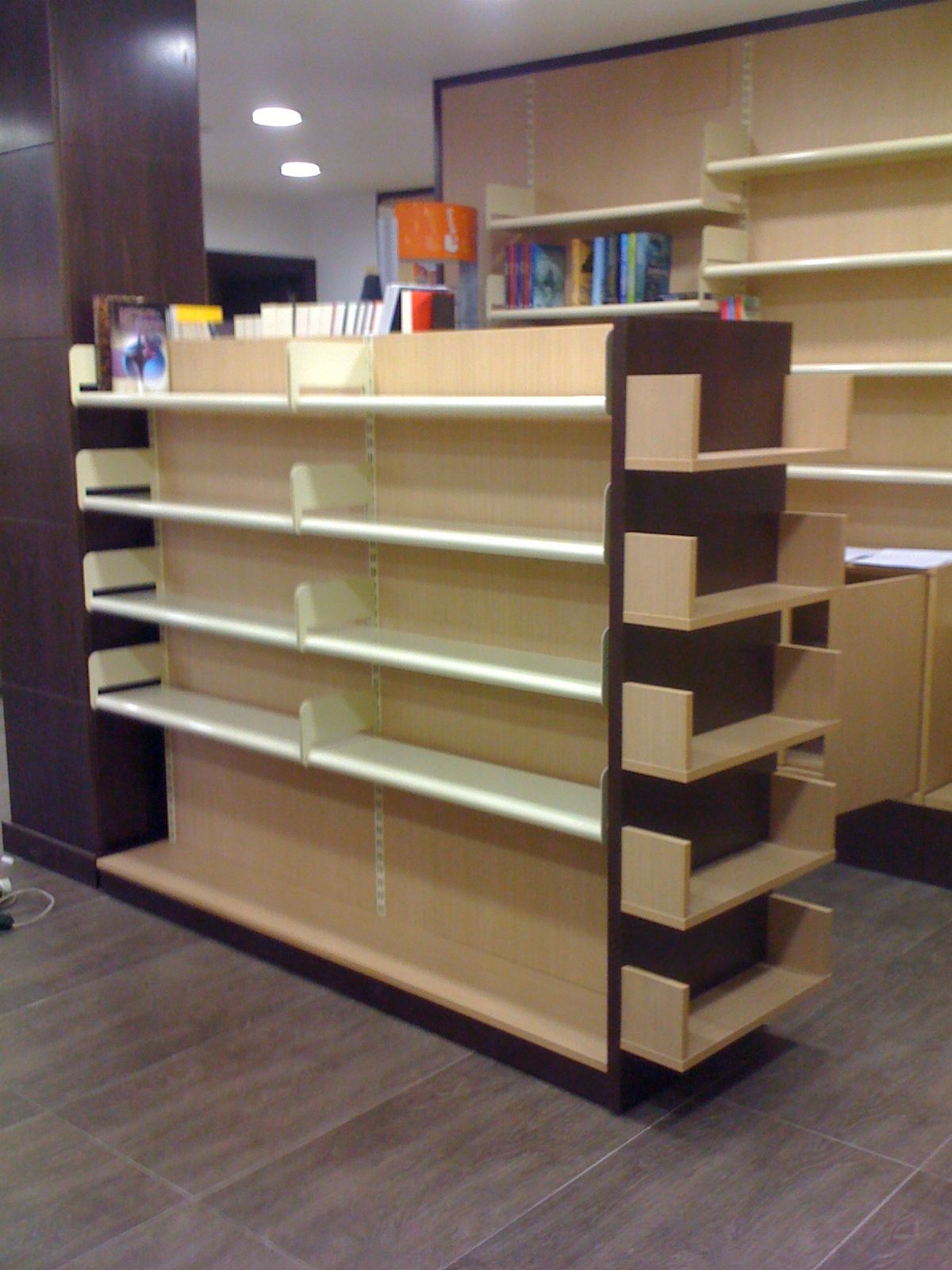 Estantería vacía de color beige con detalles de madera oscura en un pasillo de una tienda.