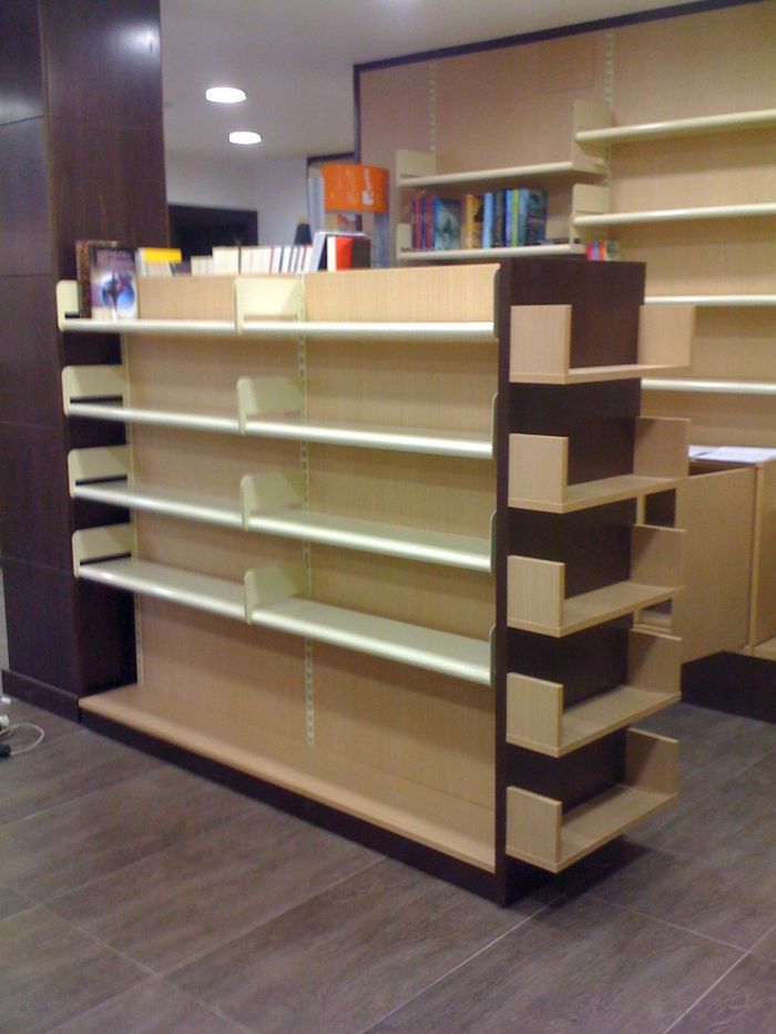 Estantería de madera vacía en el pasillo de una biblioteca o librería, con suelo oscuro y libros encima.