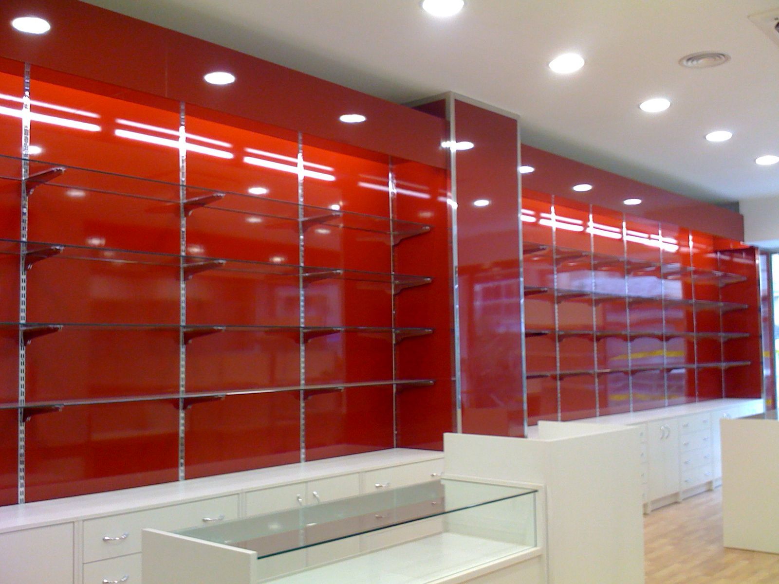 Interior comercial moderno y vacío con estanterías rojas brillantes en la pared y mostradores blancos.