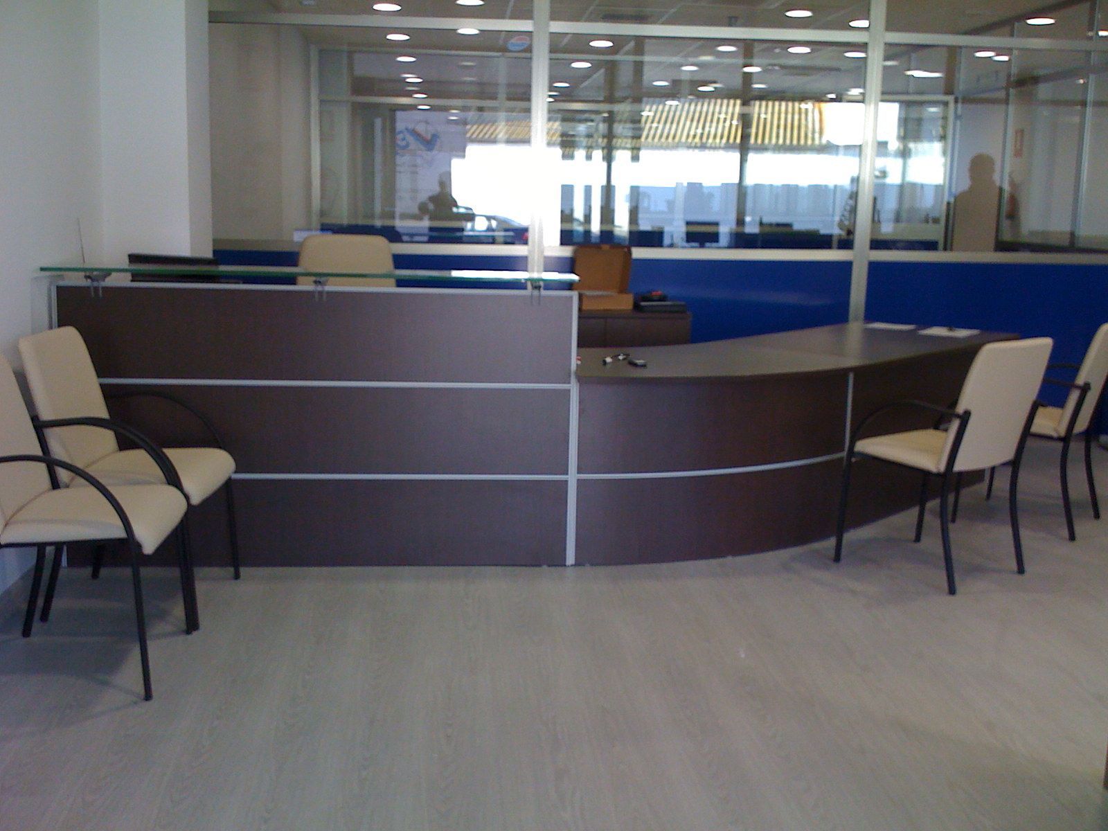 Vestíbulo de oficina vacío con mostrador de recepción curvo y sillas detrás de una pared de cristal.
