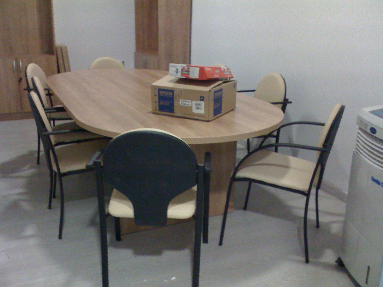 Sala de reuniones de oficina con mesa ovalada, cuatro sillas y cajas apiladas en el centro.