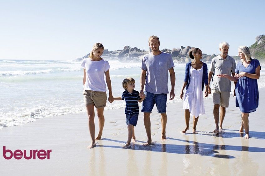 Eine Gruppe von Menschen geht am Strand spazieren, im Hintergrund ist Beurer zu sehen