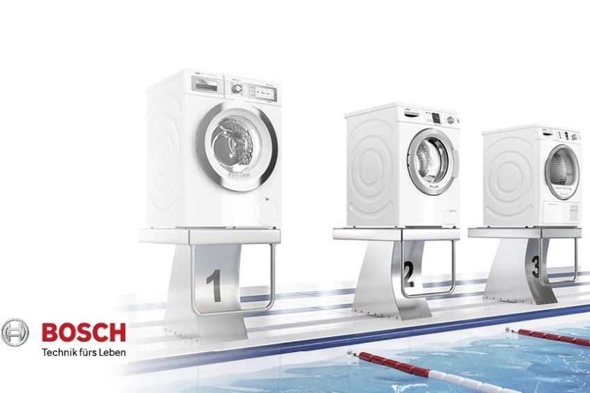 Drei Waschmaschinen stehen auf einem Podium neben einem Pool.