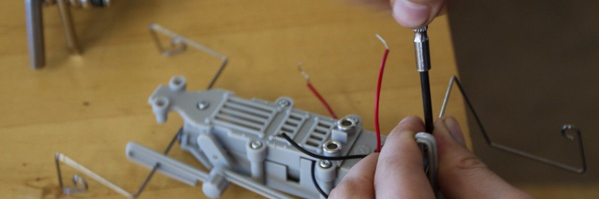 Eine Person arbeitet mit Drähten und einem Schraubenzieher an einem Roboter.