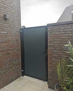 Neben einer Backsteinmauer steht ein schwarzes Tor.