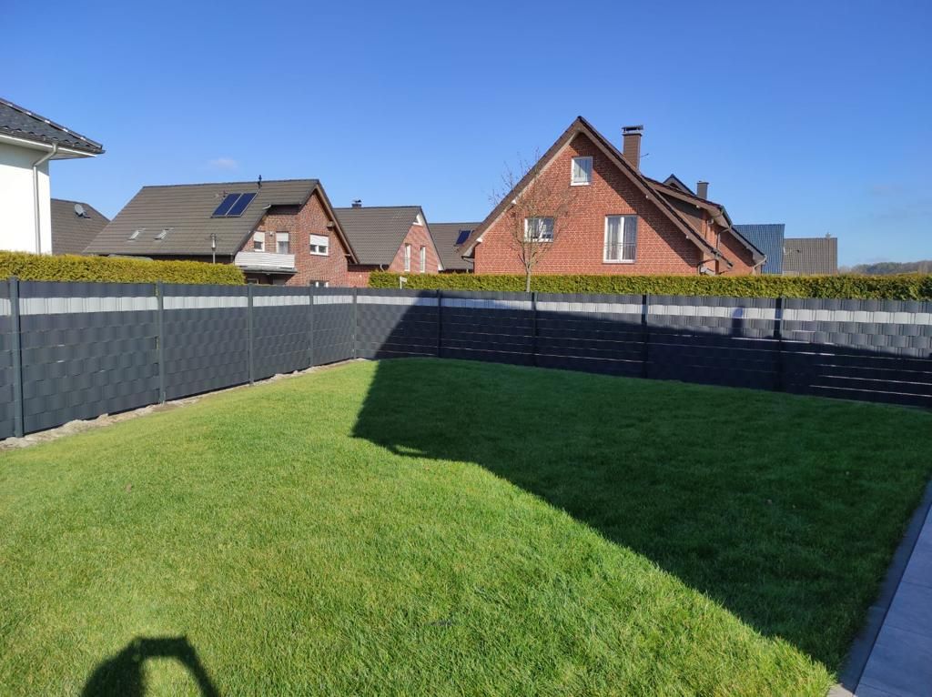 Ein Zaun umgibt einen üppigen grünen Rasen mit Häusern im Hintergrund