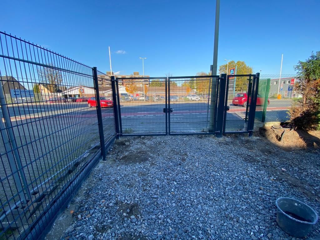 Ein Zaun mit einem Tor inmitten einer Kiesfläche.