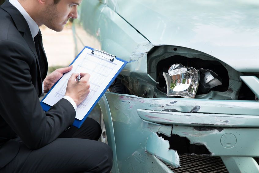 Un hombre con traje escribe en un portapapeles delante de un coche averiado.