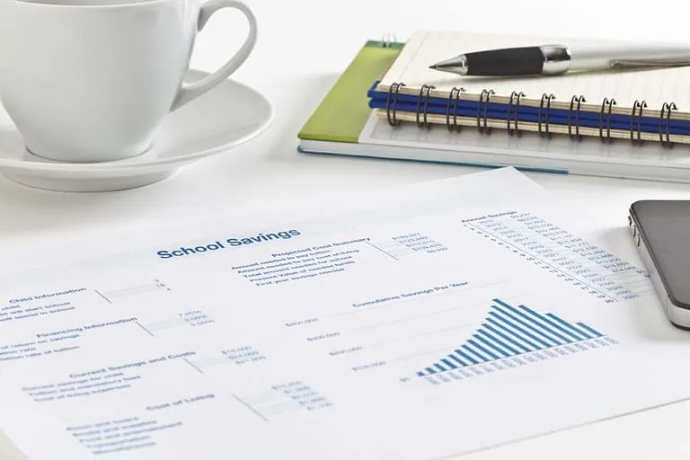 Una taza de café reposa en un platillo junto a un cuaderno y un teléfono celular.