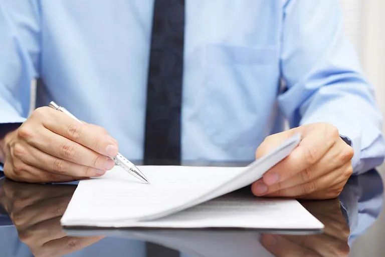 Un hombre está escribiendo en un trozo de papel con un bolígrafo.