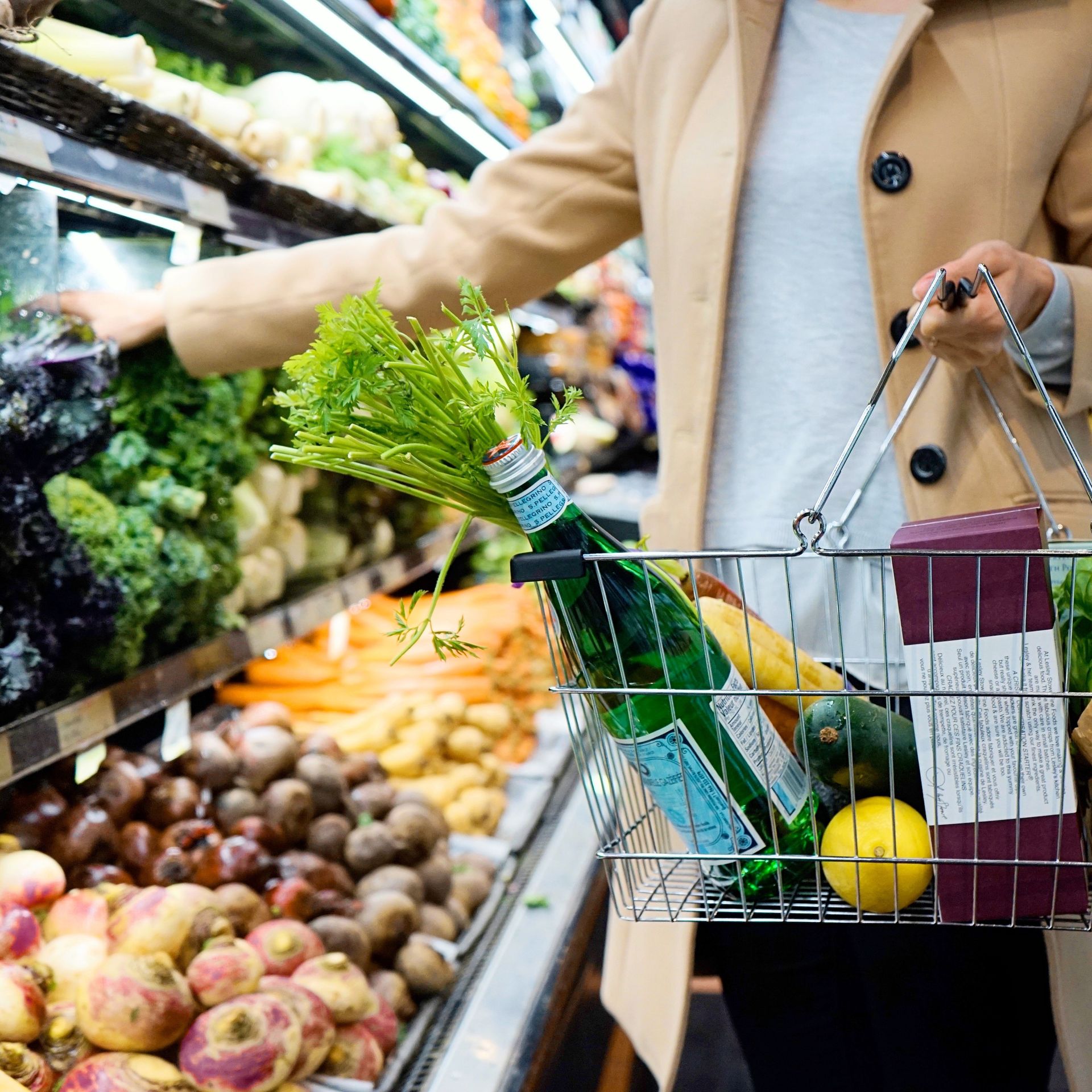 Osoba robiąca zakupy warzyw w supermarkecie, trzymająca wózek ze świeżymi produktami.