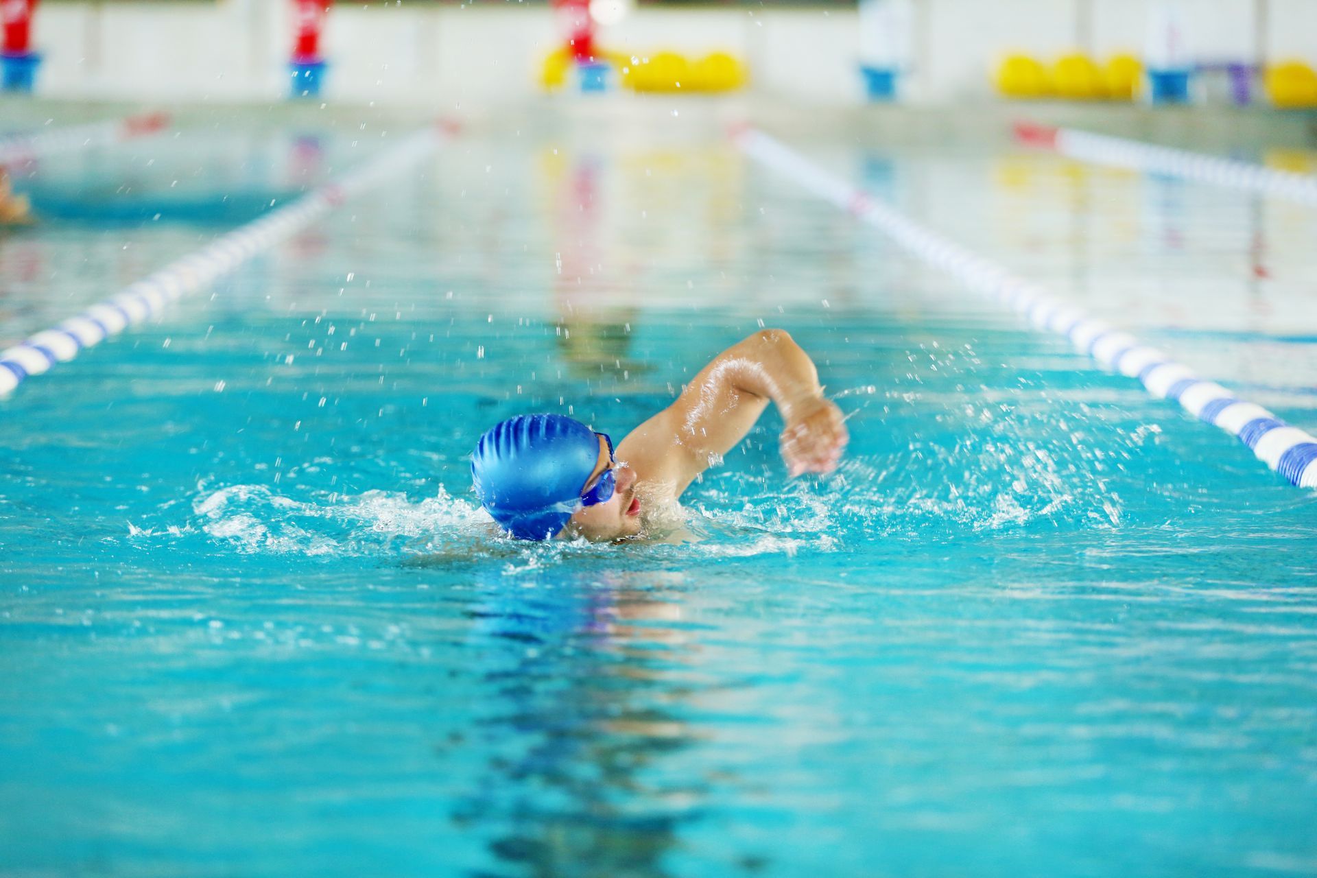 Schwimmer mit blauer Badekappe schwimmt Freistil in einem Hallenbad mit Bahnmarkierungen.